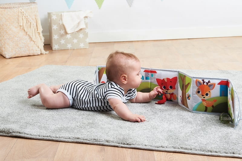 Dziecko leży na brzuszku na dywanie i ogląda dwustronną książeczkę