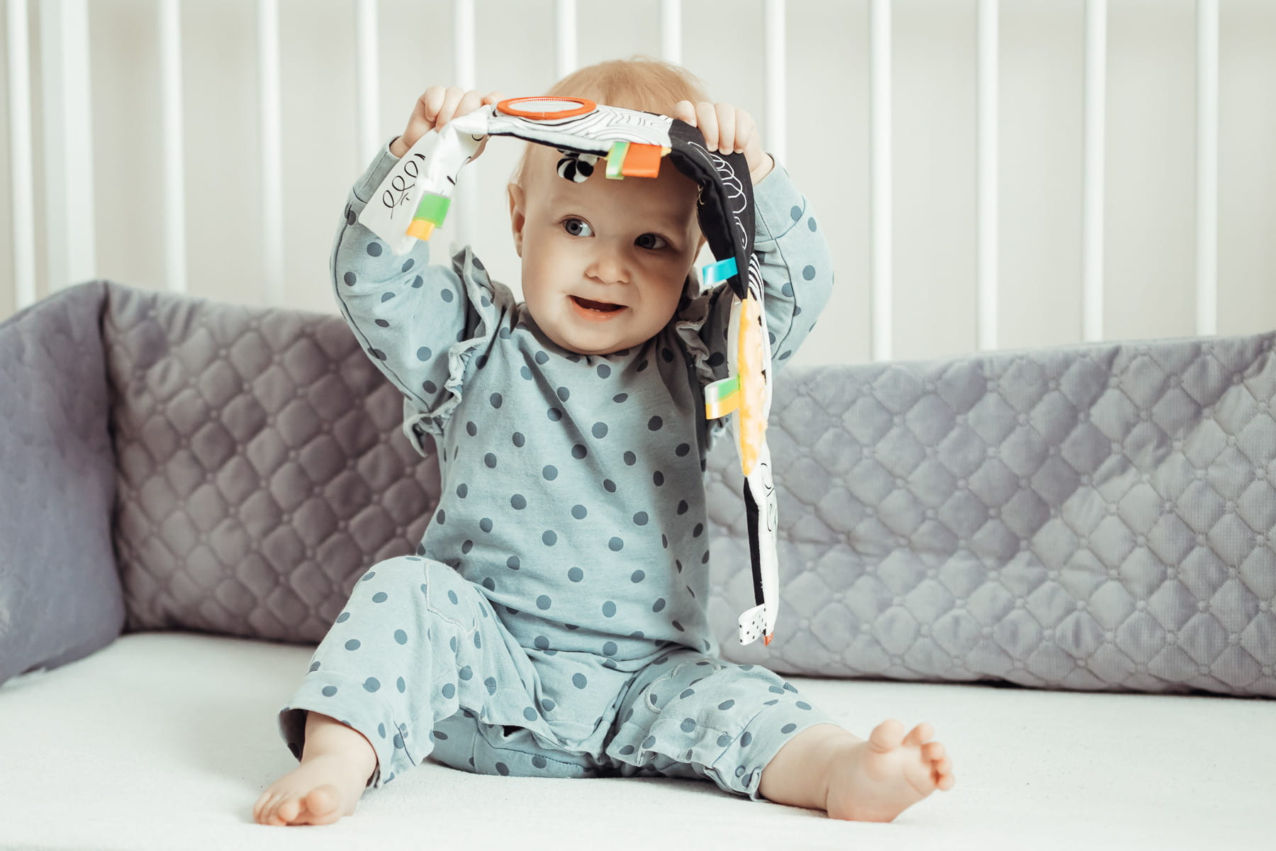 Dziecko z książeczką multisensoryczną siedzi w łóżeczku