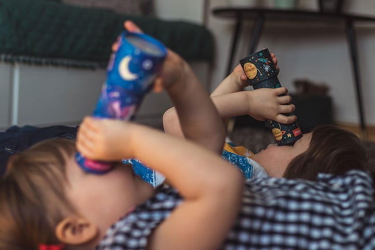 Dzieci leżą na podłodze i patrzą przez kalejdoskopy