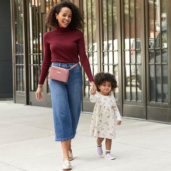 Kobieta idzie z dzieckiem za rękę - na biodrach ma nerkę torebkę w kolorze brudnego różu