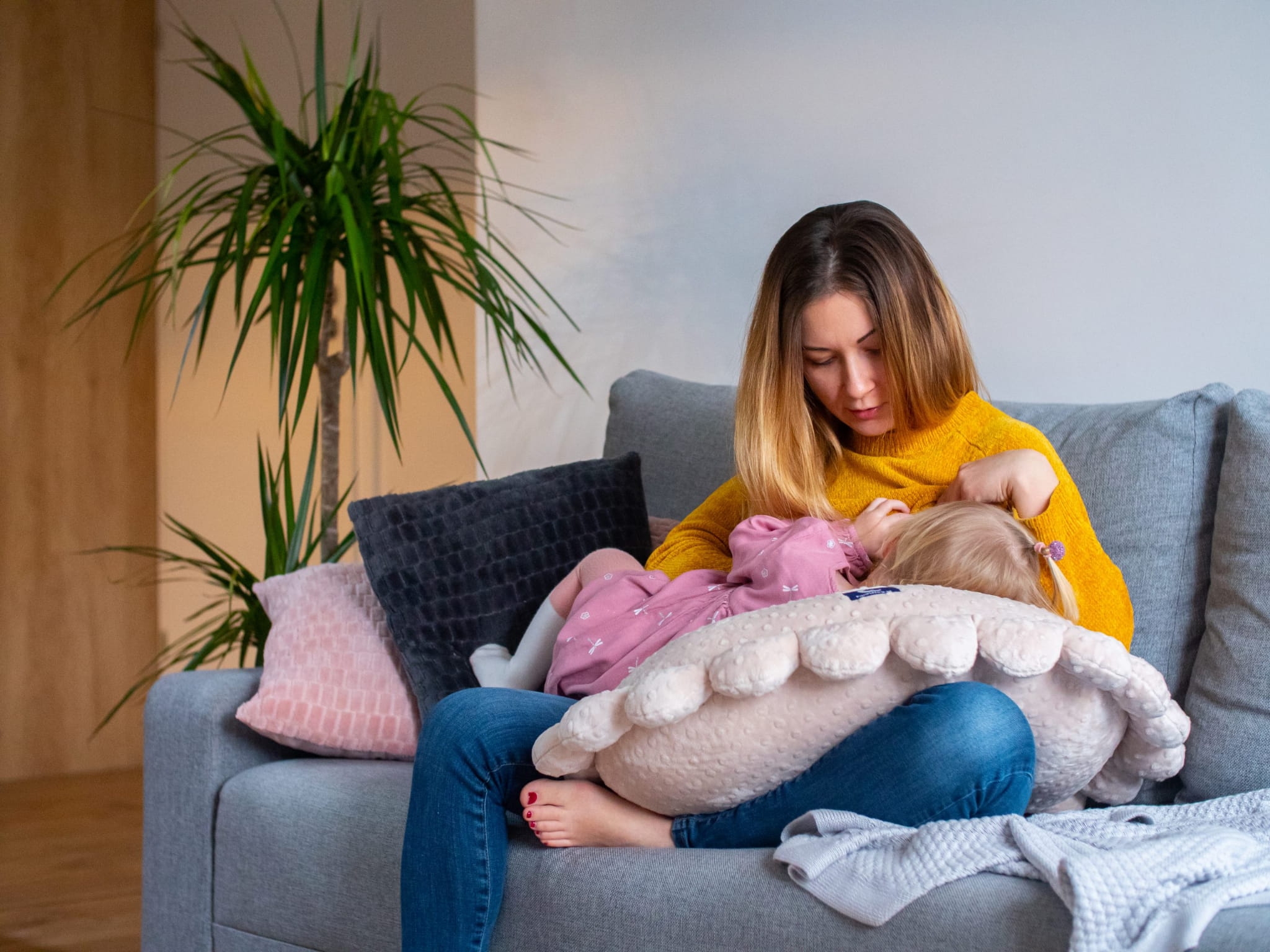 Kobieta siedzi na kanapie i karmi córkę leżącą na poduszce do karmienia
