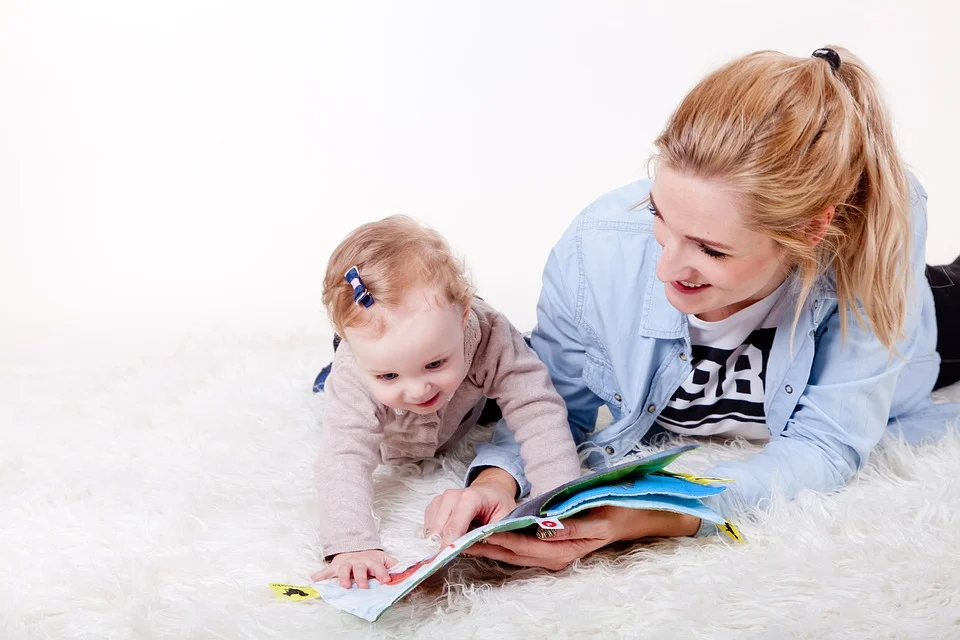 Mama blondynka i dziecko - dziewczynka czytają książeczkę na leżąco