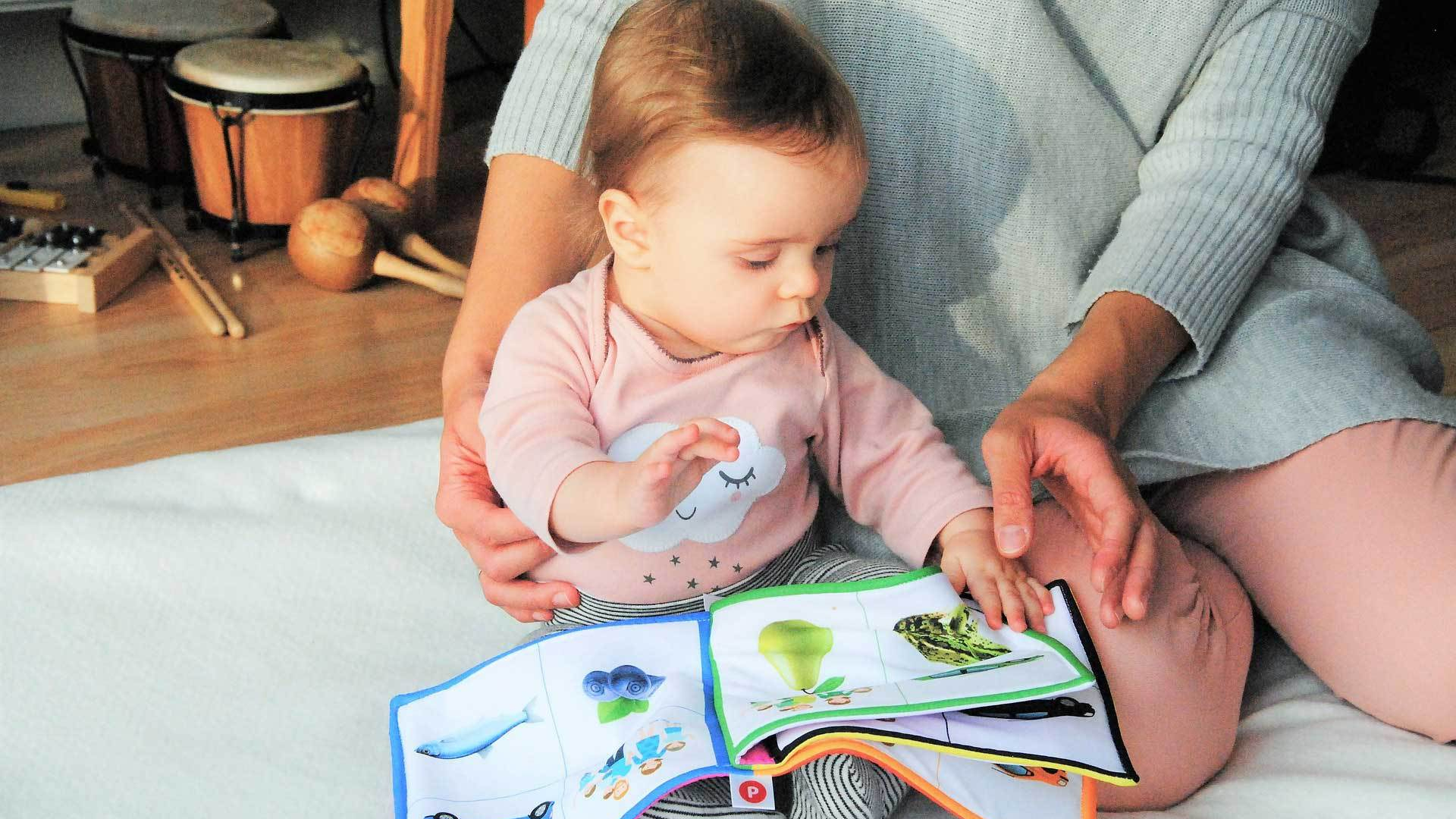 Dziecko siedzi z mamą na łóżku i ogląda książeczkę