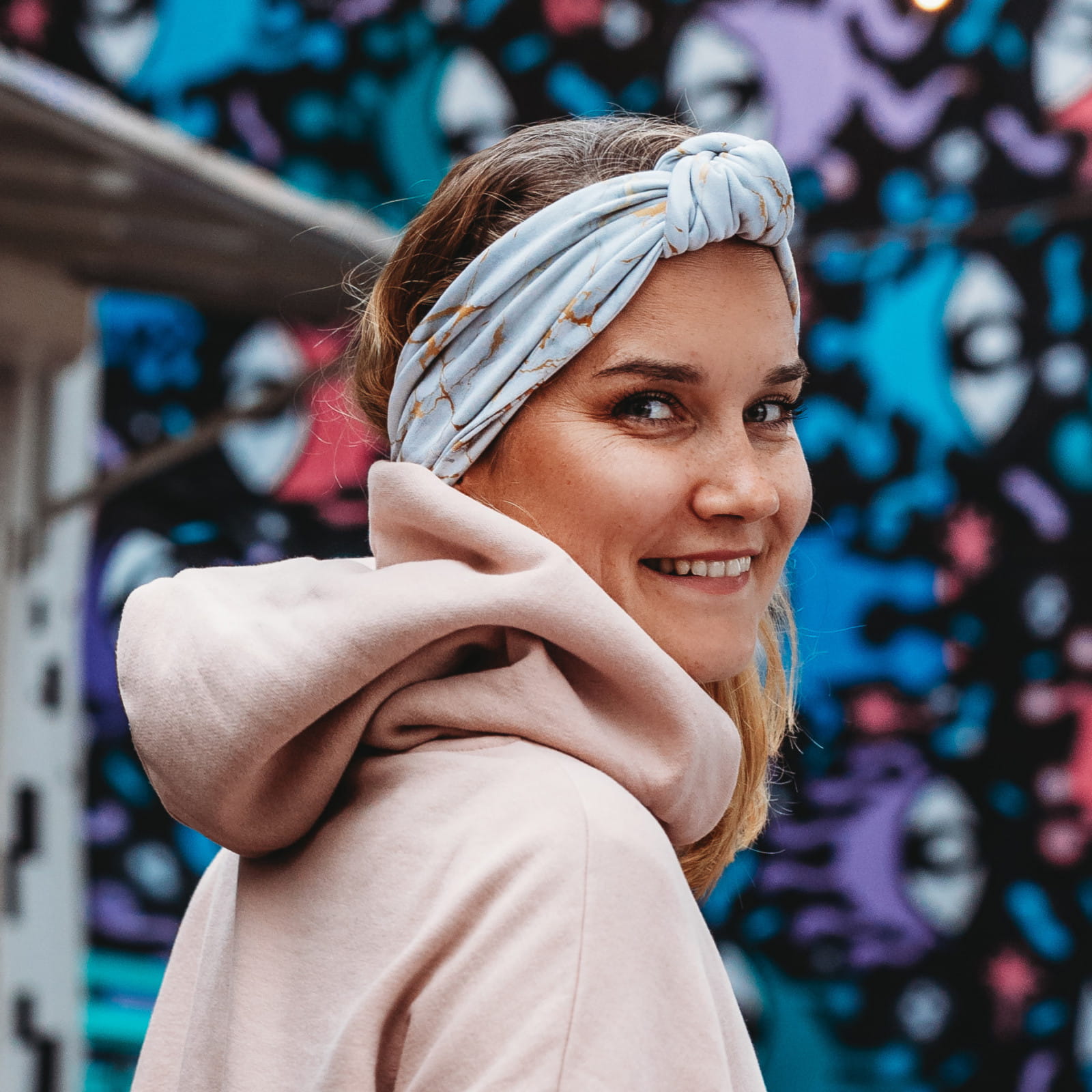 Kobieta, blondyna w pudrowej bluzie patrzy z uśmiechem w obiektyw. Na głowie ma opaskę