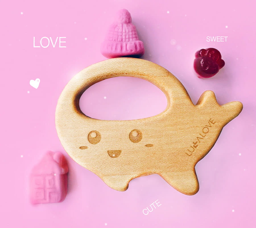 Drewniany wieloryb na różowym tle. Obok gryzaka leżą różowe słodkości